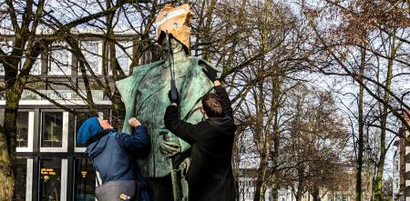 Zwei Aktivist.innen setzen einer Statue eine Papiertüte auf den Kopf