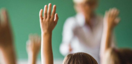 Aufzeigende Hände vor einer Tafel und einem Lehrer.