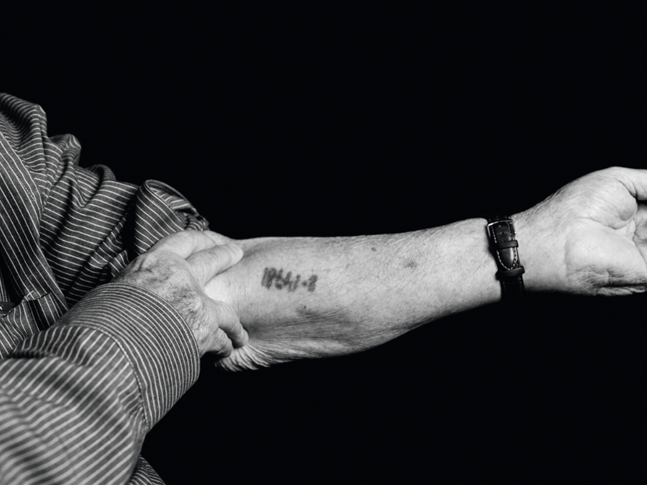 A survivor shows his arm with an inmate number tattooed on it