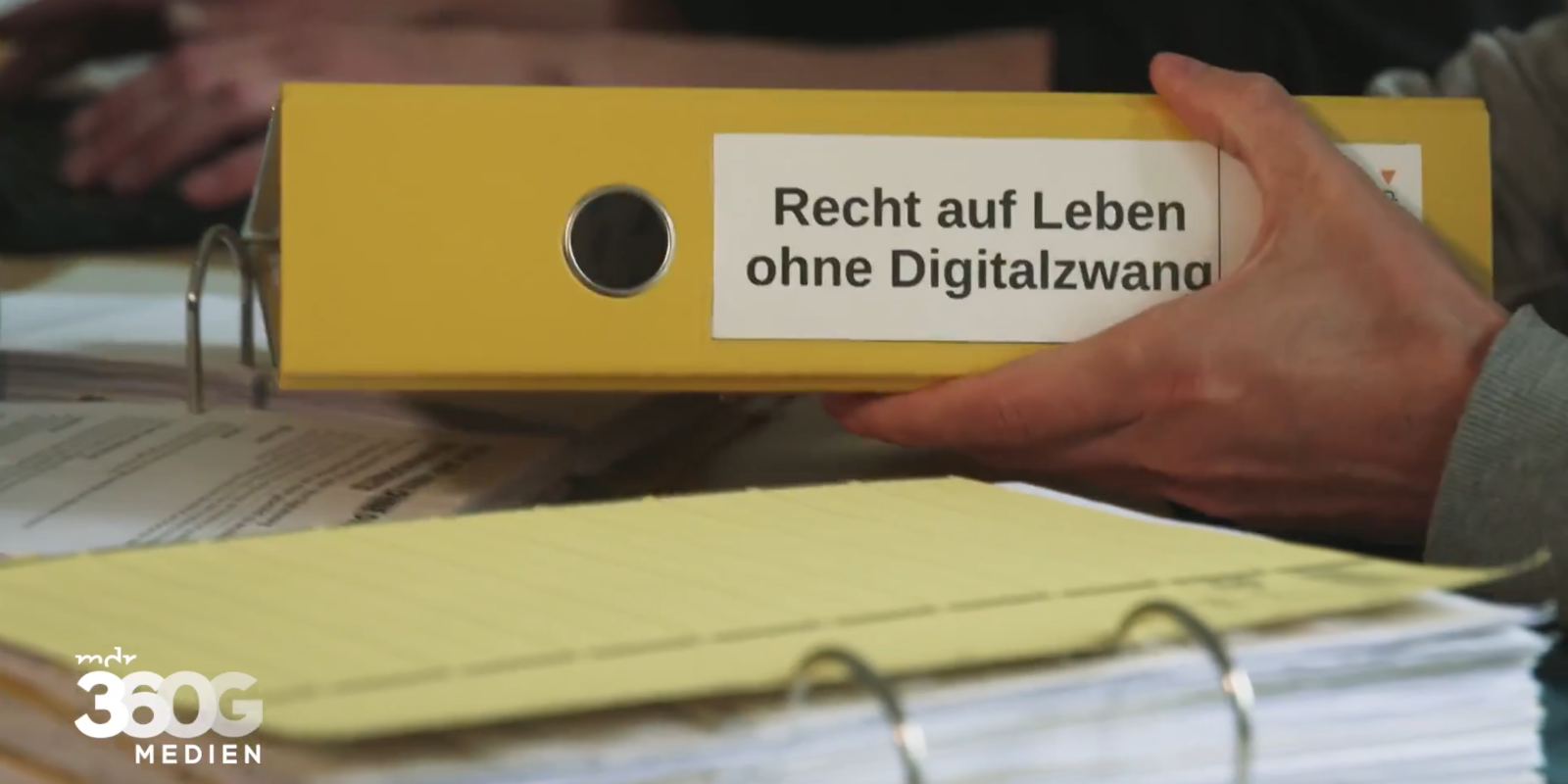 Bildausschnitt einer Reportage über Digitalzwang. Abgebildet ist ein gelber Aktenordner mit der Aufschrift „Recht auf Leben ohne Digitalzwang“