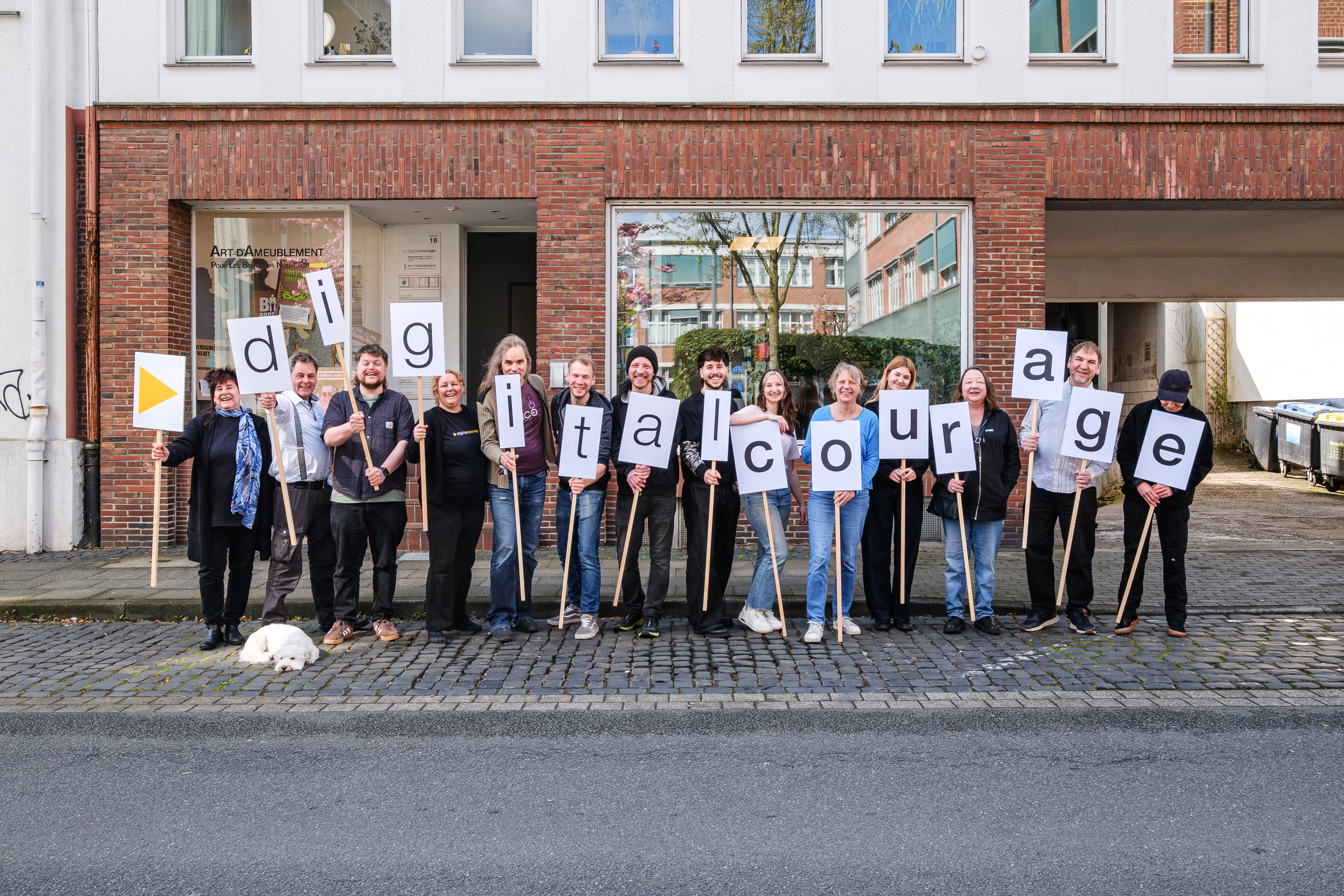 Das Team von Digitalcourage steht vor einem Backsteinhaus und hält Schilder, die zusammen den Schriftzug Digitalcourage bilden.