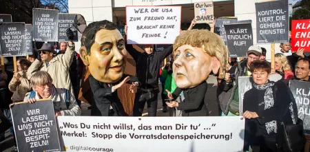 Aktivist.innen mit diversen Bannern. Im Hintergrund Pappmaché-Köpfe von Angela Merkel und Sigmar Gabriel.
