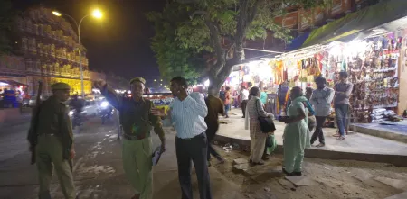 Polizei in Indien zeigt in eine Richtung. Daneben steht eine Person. Im Hintergrund sind Straßengeschäfte.