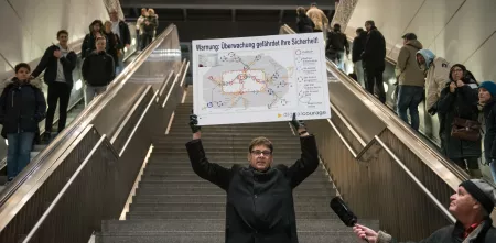 padeluun am Südkreuz mit einem Schild in der Hand: „Warnung: Überwachung gefährdet Ihre Sicherheit!“
