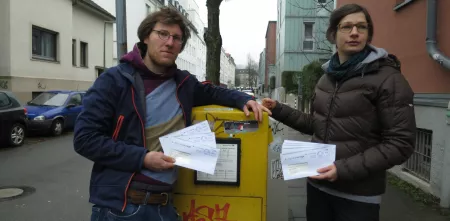 Offener Brief an VW, Uvex, AvD und Co: „VW muss Kinder-Tracking stoppen!“ Schutzranzen. Friedemann und Kerstin mit Briefen in der Hand vor einem Briefkasten.