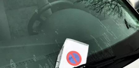 Ein Strafzettel, der hinter einem Scheibenwischer hängt.