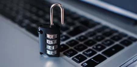 Nahaufnahme einer Tastatur. Darauf steht ein geöffnetes Sicherheitsschloss.