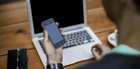 Eine Person an einem Laptop, die gleichzeitig auf ein Smartphone schaut.