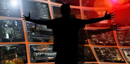 Eine Silhouette einer Person die vor einer Vielzahl von Monitoren steht.