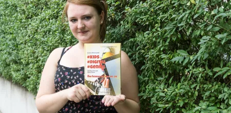Jessica Wawrzyniak hält ihr Buch #Kids #digital #genial in den Händen und präsentiert es der Kamera.