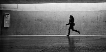 Eine Person, die, an einer Bahnstation, von rechts nach links rennt (Aufnahme in schwarz-weiß).