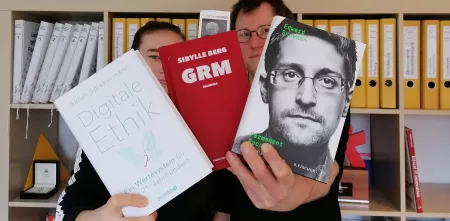 Zwei Personen halten drei Bücher Richtung Kamera: Digitale Ethik, GRM und Edward Snowden