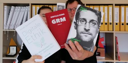 Zwei Personen halten drei Bücher Richtung Kamera: Digitale Ethik, GRM und Edward Snowden