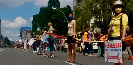Eine Reihe von Demonstrationsteilnehmer.innen mit 1,5 Metern Sicherheitsabstande stehen auf der Straße