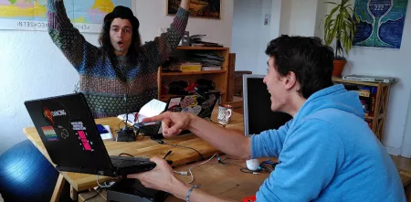 Trainer.innen Adrian und Robin Grimm (Die Gebrüder Grimm) jubelnd-freudig an einem Laptop.