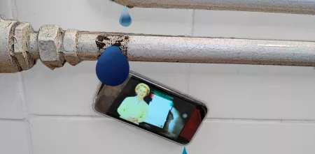 Das Bild zeigt zwei alte Leitungsrohre mit einem Wasserleck. Wasser tropft von den Rohren und entlang eines Smartphones. Auf dem Smartphone ist die EU-Kommissionspräisdentin Ursula von der Leyen zu sehen vor dem Hintergrund eines großen Smartphones.