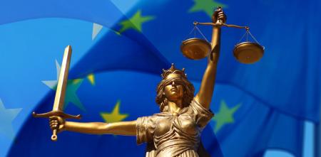 Justitia mit Schwert und Waage in Händen vor blauer EU-Flagge.