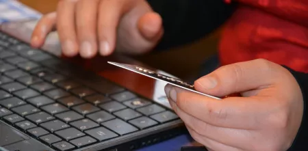 Hände, die Kreditkarte halten und Tastatur im Hintergrund.