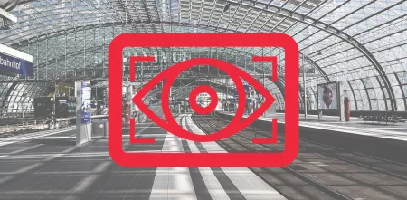 Rotes Kampagnenlogo mit einem stilisierten Auge. Im Hintergrund eine große Bahnhofshalle. 