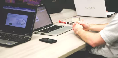Foto von mehreren Personen, die mit ihren Laptops um einen hölzernen Tisch sitzen