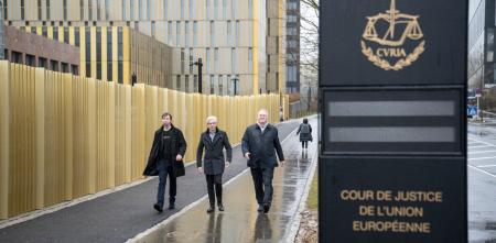  Three people are walking towards the camera. In the right of the picture there is a sign indicating the Court of Justice of the European Union.