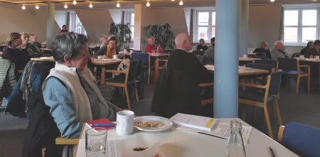 An meherern Tischen sitzen Leute und schauen nach vorne, auf den Tischen stehen Teller mit Kuchenkrümeln und Kaffeetassen