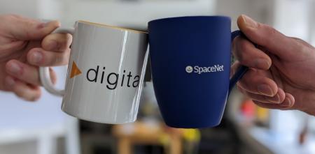 Die Hände von zwei Personen sind zu sehen, die mit Kaffeebechern anstoßen. Auf dem rechten, blauen Becher ist das Logo der SpaceNet AG zu sehen, auf dem linken, weißen Becher das Logo von Digitalcourage.