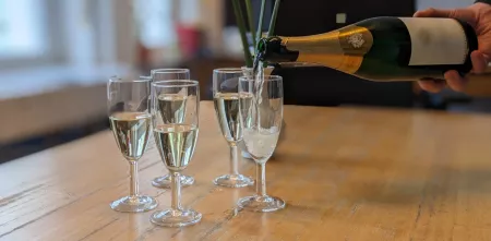 Mehrere Sektgläser stehen gefüllt auf einem Tisch. Das letzte verbleibende Sektglas wird gerade mit einer Sektflasche befüllt.