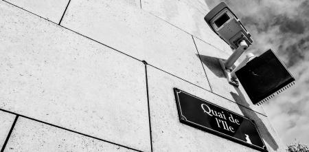 Detailaufnahme einer Gebäudeecke mit Straßenschild. Darüber eine Überwachungskamera.