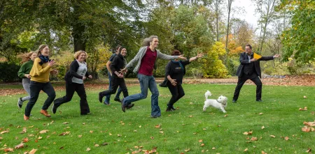 Ein paar Leute und ein Hund laufen mit viel Elan über eine Wiese in die Richtung, die ein Digitalcourage-Dreieck angibt