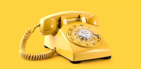 Ein gelbes Wählscheibentelefon vor gelbem Hintergrund.