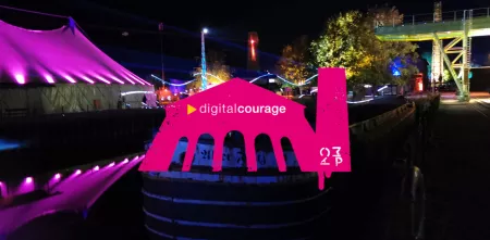 im Hintergrund Atmo von einem Chaos Communication Camp. Im Vordergrund ein neonpinkes Zelt mit Digitalcourage-Logo
