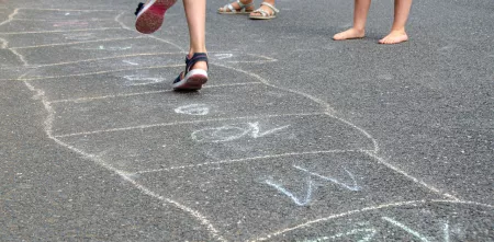 Kinder spielen und hüpfen über mit Kreide gemalte Quadrate.