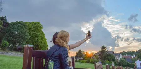 Zwei Frauen machen ein Selfie auf einer Parkbank. Im Hintergrund blauer Himmel mit Wolken und Abendröte.