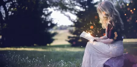 Ein Mächen sitzt auf einer Wiese und liest ein Buch, aus dem Funken sprühen