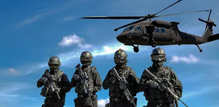 Vier Personen mit Schutzausrüstung und Gewehren. Im Hintergrund ein Hubschrauber vor blauem Himmel.