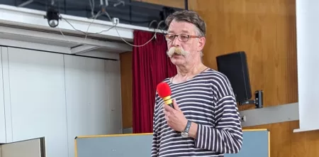 Albrecht Ude bei einem Vortrag mit einem Mikrofon in der Hand.