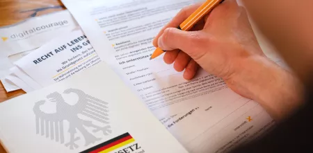 Eine Person ist dabei, die Petition zu unterzeichnen. Neben der ausgedruckten Petition liegt das Grundgesetz.