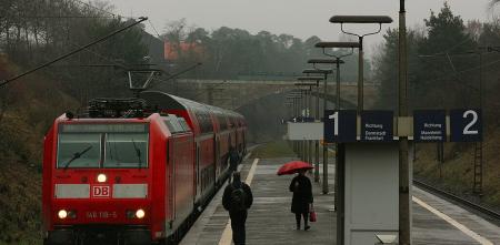 Ein roter Regionalzug an einem unüberdachten Haltepunkt an einem regnerischen Tag