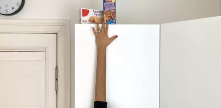 Foto eines Arms, der mit Hilfe eines Grafikprogramms künstlich verlängert wurde, um an Kekse zu kommen, die auf einem hohen Schrank stehen.