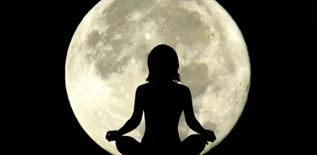 Mond vor schwarzem Himmel, davor eine schwarze Frauensilhouette in entspanntem Schneidersitz. Die Arme sind wie bei einer Meditation auf den Knien abgelegt.