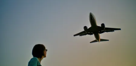 Froschperspektive: Silhouette eine Person. Darüber in der Ferne ein Flugzeug.