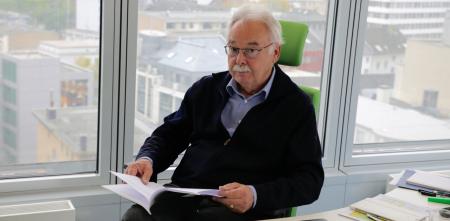 Prof. Thomas Feltens sitzt an einem Schreibtisch mit einem aufgeschlagenem Heft in der Hand.