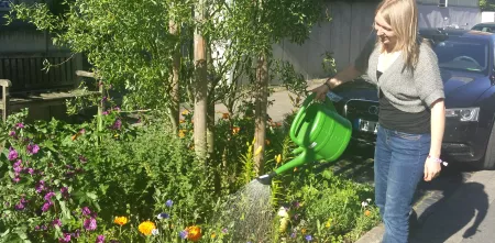 Praktikantin gießt die Blumen auf dem Straßenbeet gegenüber unseres Büros.