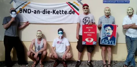 Mehrere Personen mit Gesichtsmasken stehen in einer Reihe. Sie halten Plakate und Banner in den Händen.