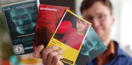 Eine Person, die Flyer und eine DVD (Citizenfour) Richtung Kamera hält: