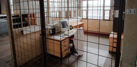 Ein Computer auf einem Schreibtisch in einer Art Zelle hinter Gittern.