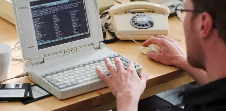 Eine Person sitzt an einem sehr alten Laptop.