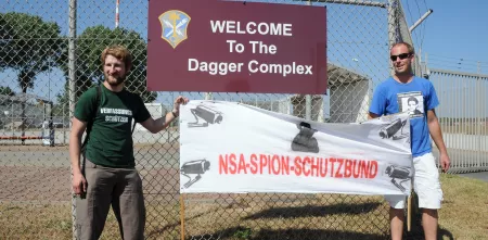 Zwei Personen halten ein Banner mit der Aufschrift: „NSA-Spion-Schutzbund“.
