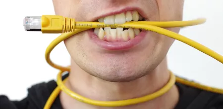 Detailaufnahme einer Person (Mundpartie), die ein gelbes Ethernet-Kabel um den Hals udn im Mund hat.